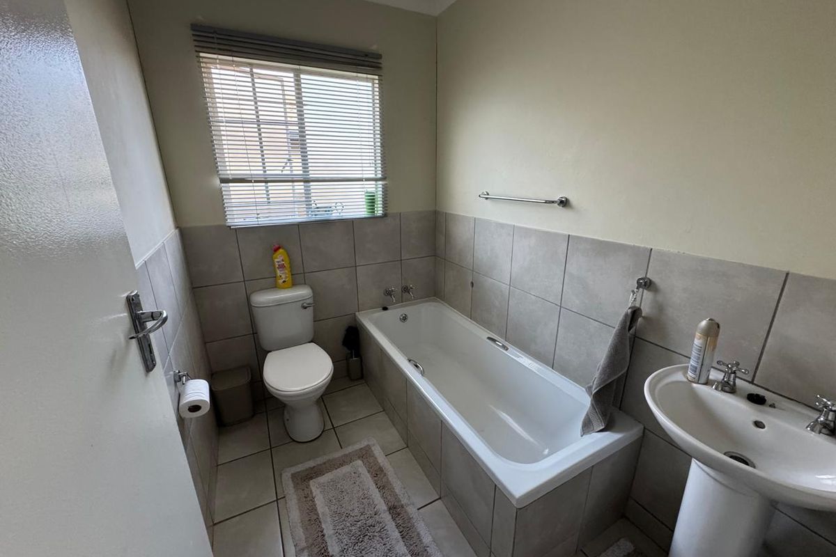 A functional bathroom featuring a bathtub, pedestal basin, toilet, and neutral tiled finishes, providing a clean and practical space.