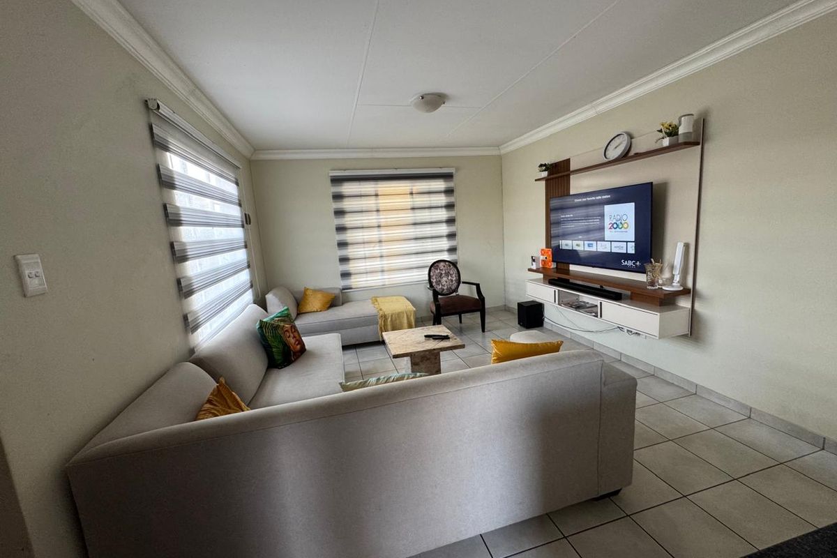 A well-maintained living room featuring tiled flooring, ceiling cornices, modern zebra blinds, and a built-in wall-mounted media console.