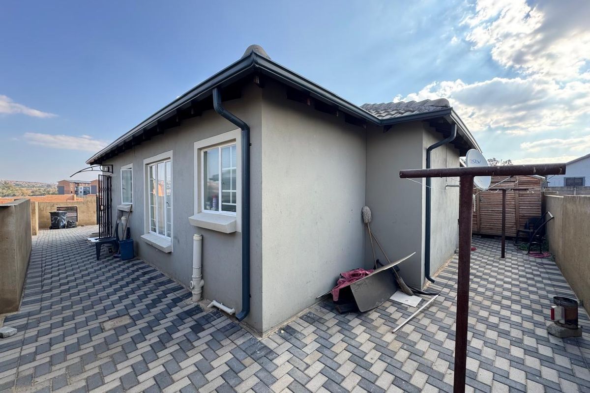 Rear exterior view of the property featuring a paved patio area, tiled roof, and perimeter boundary walls.