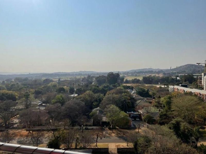 Elevated panoramic view overlooking the surrounding neighborhood, tree-lined streets, and distant landscape from an apartment balcony.