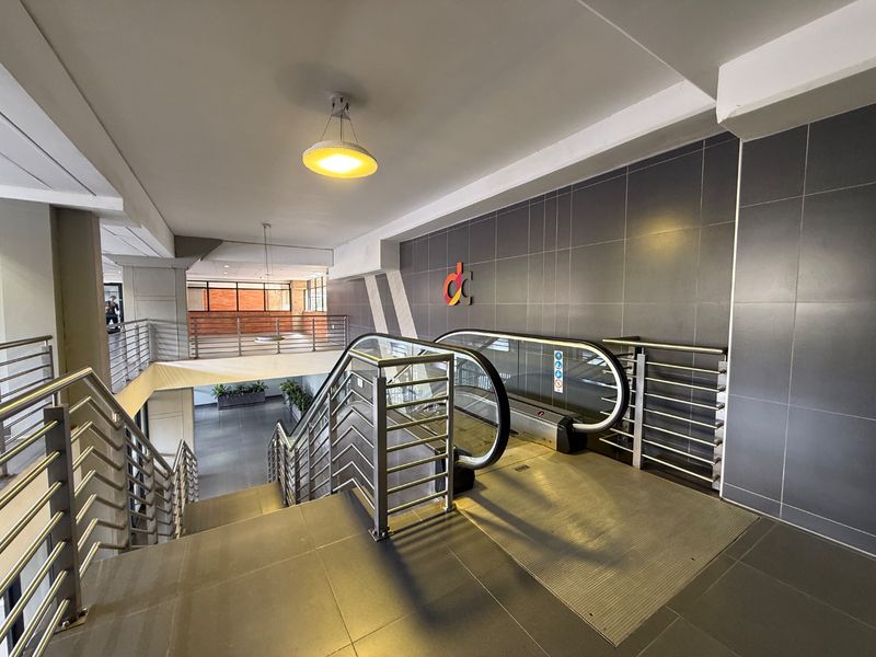 A modern commercial building interior featuring an escalator, stainless steel railings, and tiled finishes in a clean, well-maintained common area.