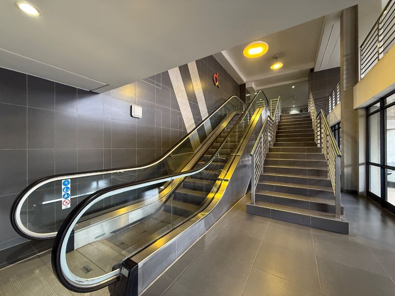 Modern apartment building entrance featuring a functional escalator and adjacent staircase with stainless steel railings and contemporary tiled finishes.