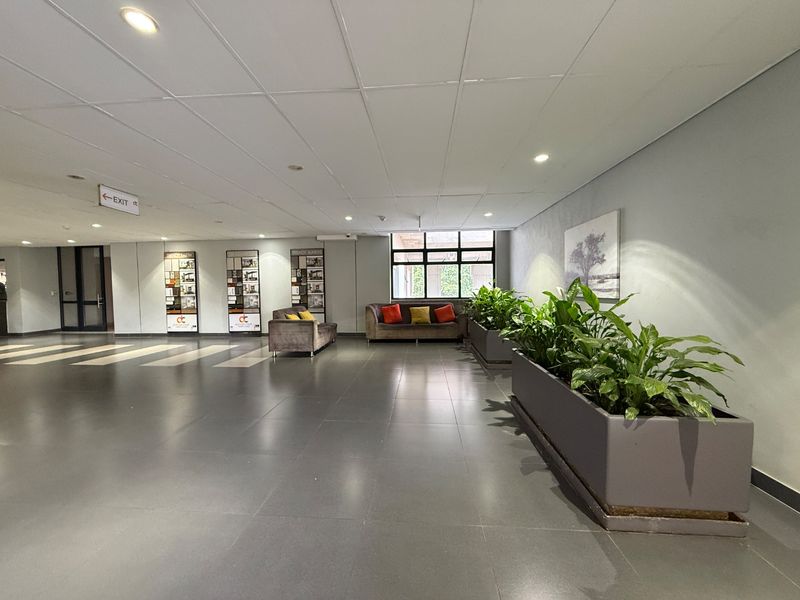 A spacious, well-lit communal lobby or clubhouse area featuring tiled flooring and a suspended ceiling, suitable for building residents.