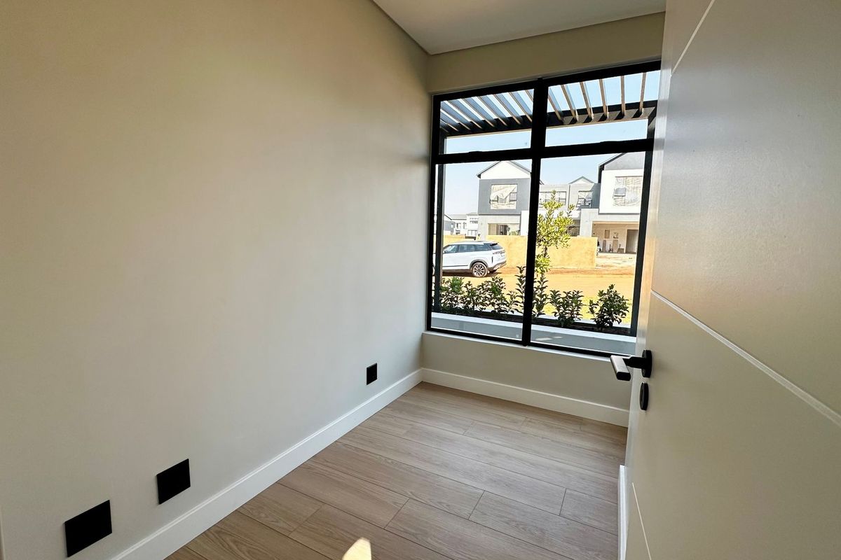 A bright, modern, and empty bedroom featuring neutral walls, wood-look laminate flooring, and a large window with views of the surrounding estate.
