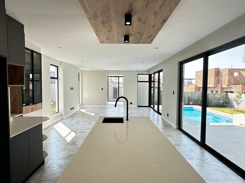 Modern open-plan kitchen and living area featuring a large island, sleek cabinetry, and expansive sliding doors opening to a pool area.