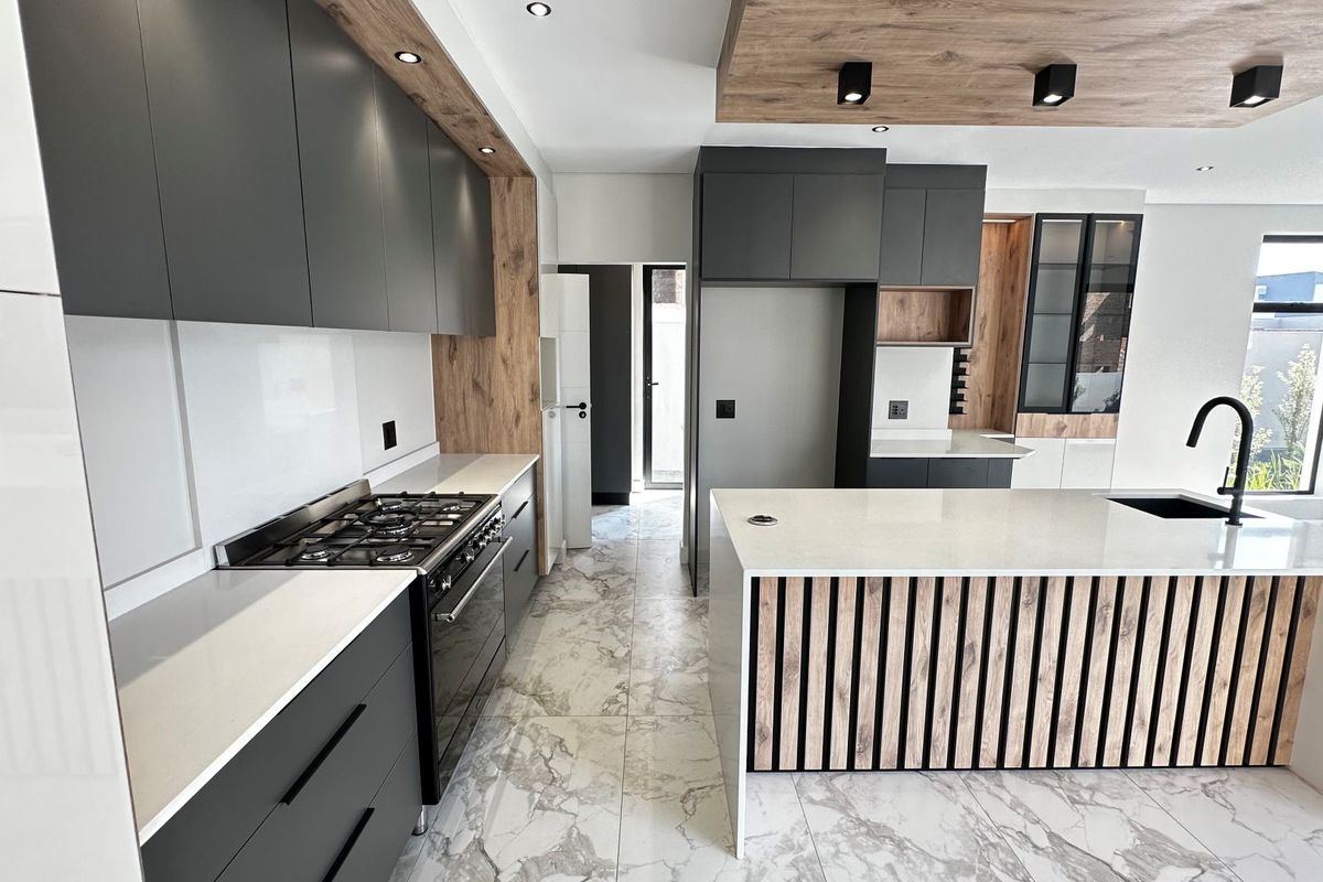 Modern kitchen featuring dark cabinetry, wood-look accents, stone countertops, a central island with a sink, and high-end built-in appliances.