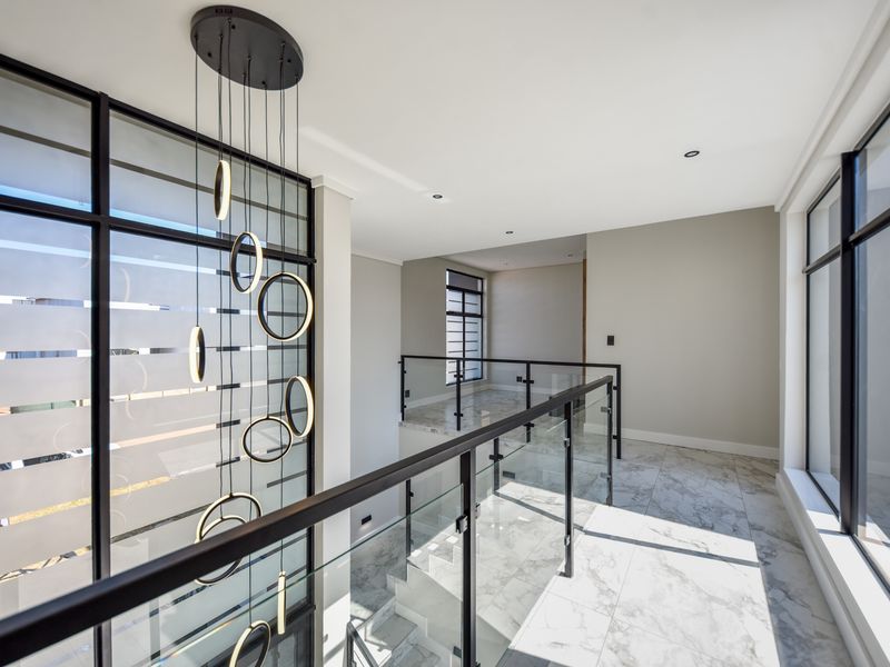 A bright, modern upper-level landing featuring marble flooring, a glass balustrade, and a striking contemporary pendant light fixture.