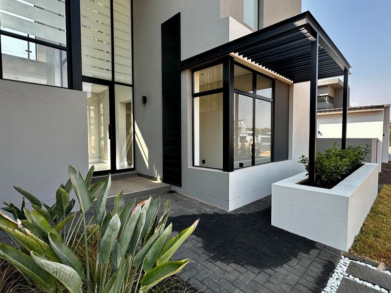 Modern architectural front entrance featuring a striking black metal pergola, large glass windows, and a clean, contemporary facade with a built-in concrete planter.