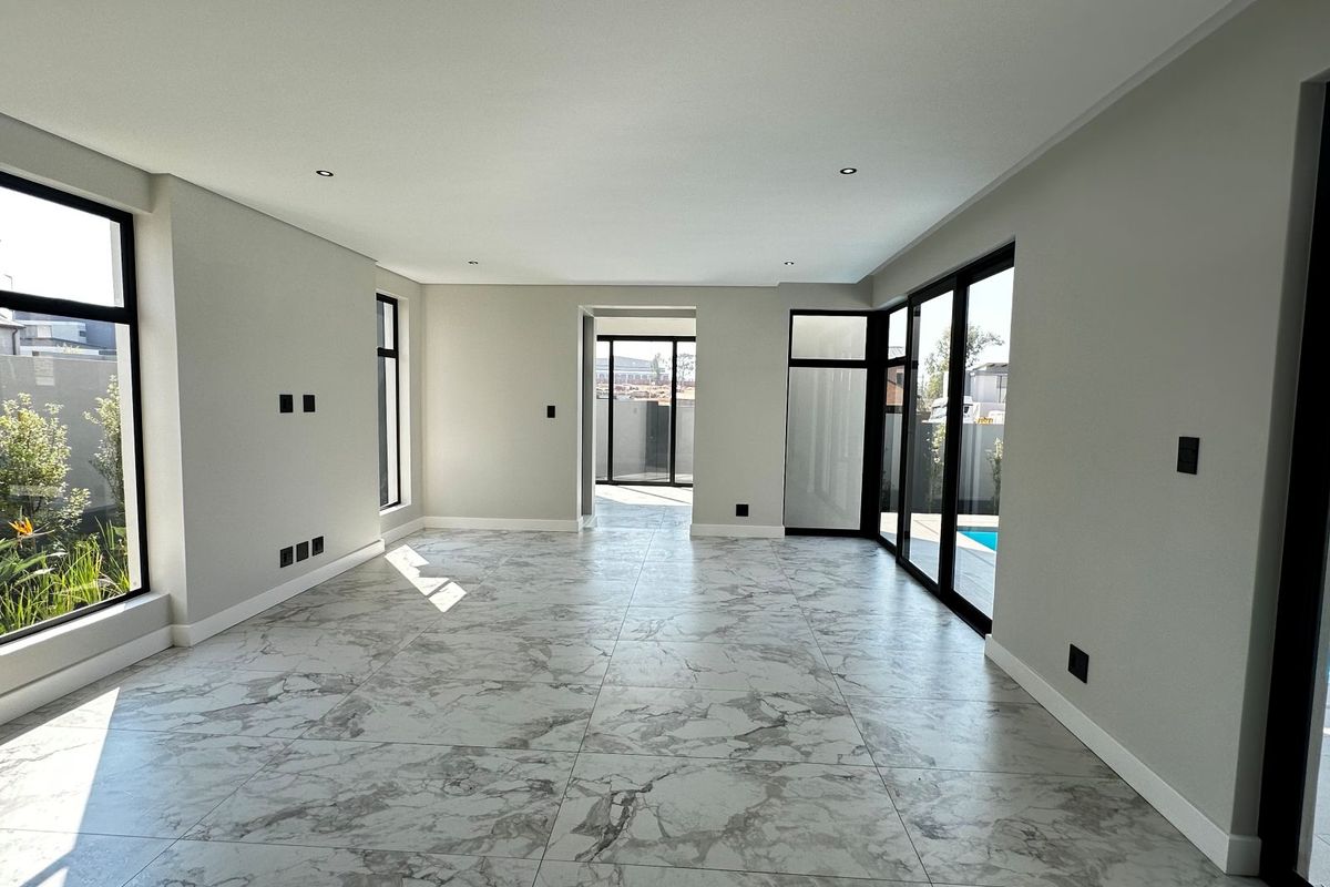 A bright, modern, and spacious open-plan living area featuring large format marble-look floor tiles, recessed lighting, and expansive black-framed glass doors leading to the pool.