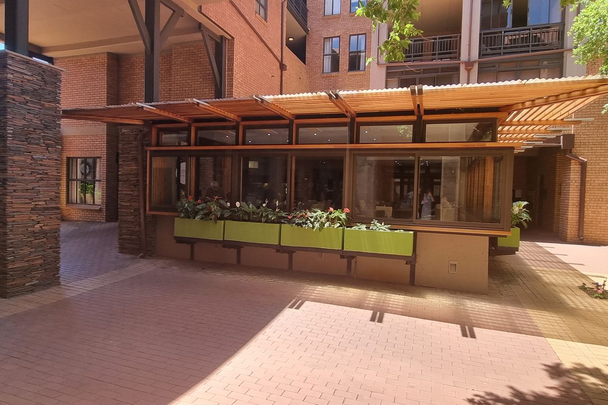 A well-maintained outdoor courtyard area featuring brick paving, stone-clad structural columns, and a timber pergola structure with integrated planter boxes.