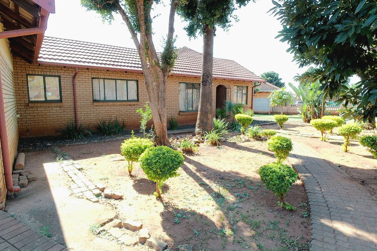 A rear view of a face brick house featuring a tiled roof, established trees, and a paved garden walkway.