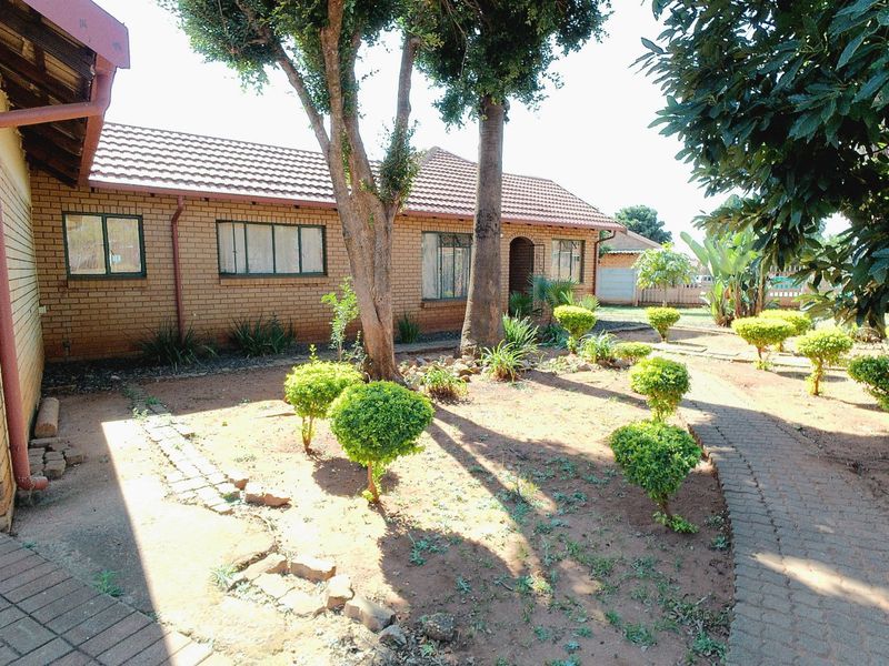 A rear view of a face brick house featuring a tiled roof, established trees, and a paved garden walkway.