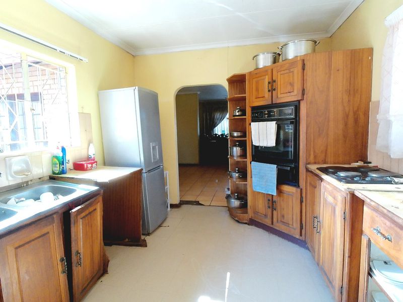 A dated kitchen featuring wooden cabinetry, built-in oven, hob, and tiled flooring, offering potential for modernization and renovation.