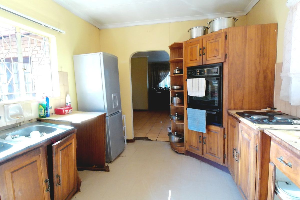 A dated kitchen featuring wooden cabinetry, built-in oven, hob, and tiled flooring, offering potential for modernization and renovation.