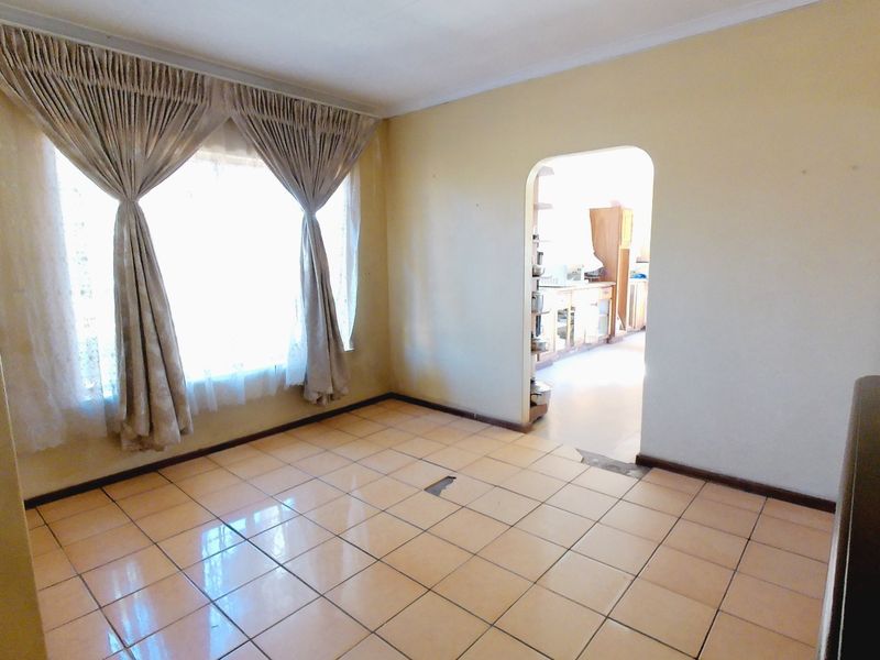 An empty living room featuring tiled flooring and an arched doorway leading to the kitchen area.