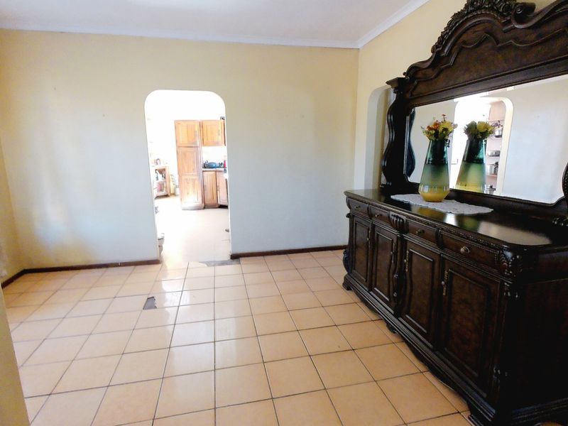 A living area featuring ceramic floor tiles and an arched doorway leading to the kitchen, showing signs of wear on the flooring.