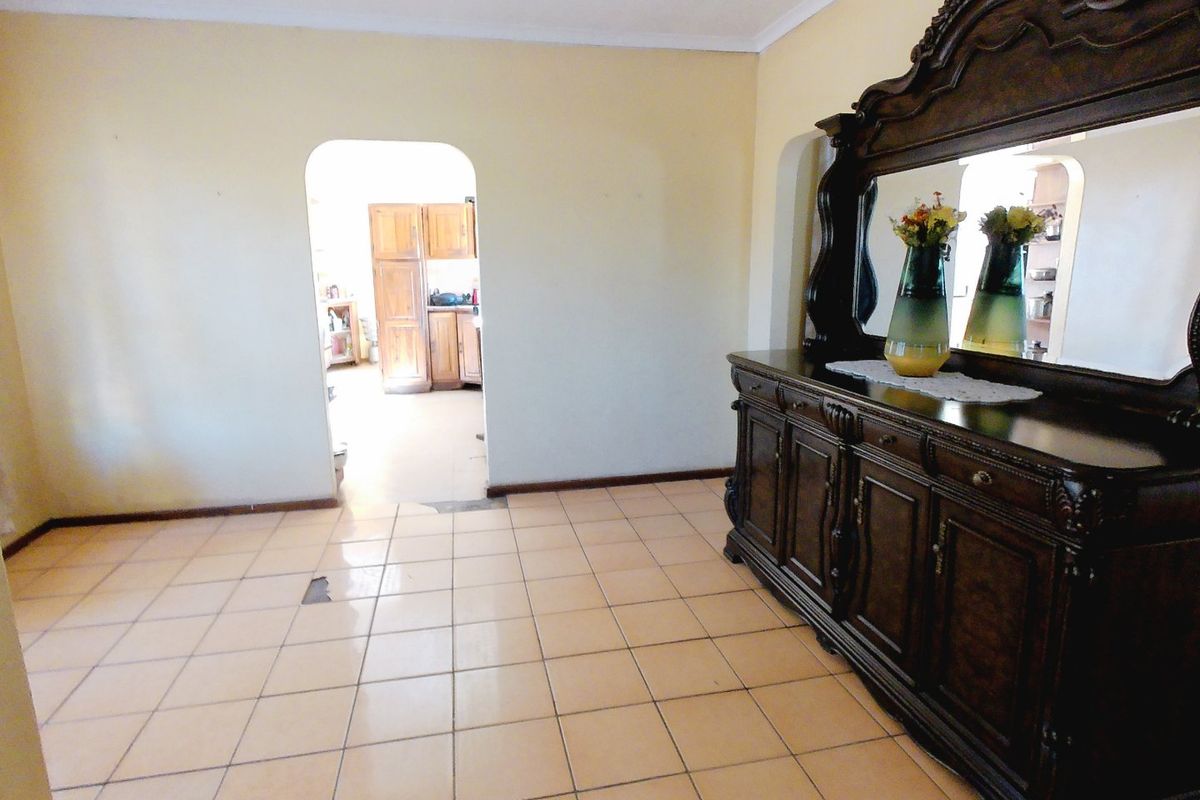A living area featuring ceramic floor tiles and an arched doorway leading to the kitchen, showing signs of wear on the flooring.