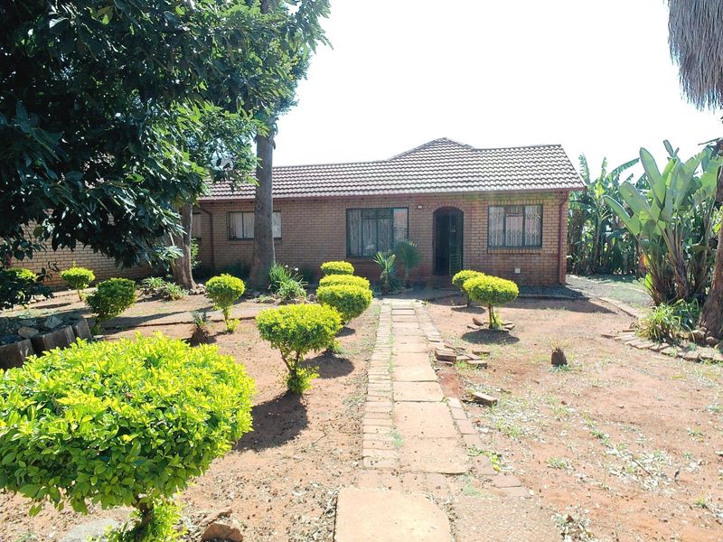 A single-story brick house featuring a tiled roof, security gates, and a paved walkway leading to the front entrance, set within a garden.