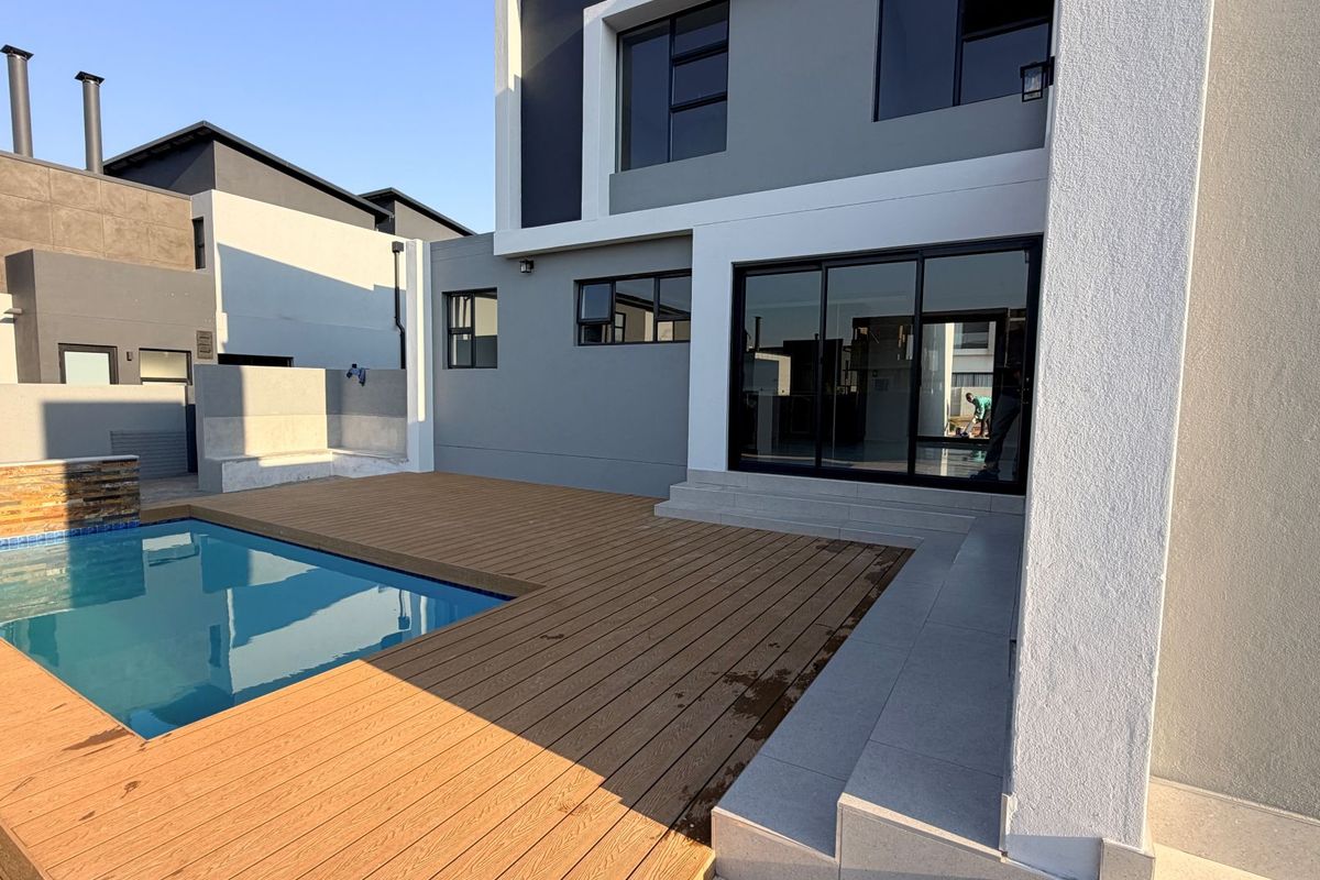 Rear exterior view featuring a modern swimming pool, timber decking, and large sliding glass doors leading into the home.