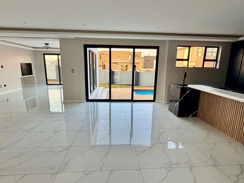 Spacious open-plan living area featuring modern marble-look floor tiles, a sleek kitchen island with stone countertops, and seamless access to the outdoor patio.