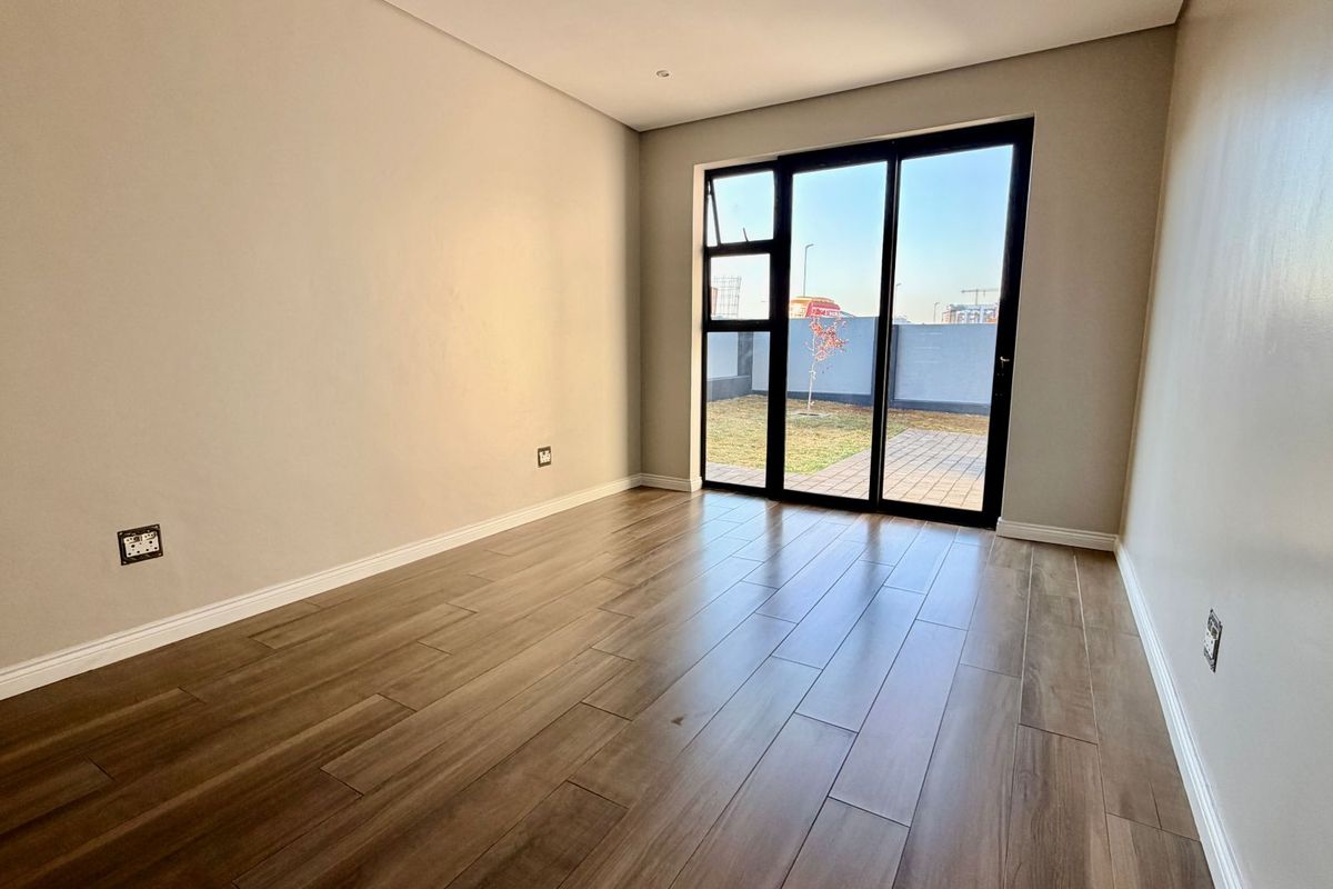 A bright, empty bedroom featuring modern wood-look tile flooring and a large sliding glass door providing access to the rear garden area.