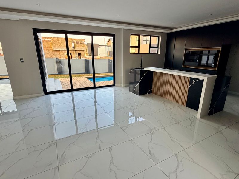 Modern open-plan living and kitchen area featuring high-gloss marble-look tiles, sleek dark cabinetry, and large sliding doors opening to a patio and pool.