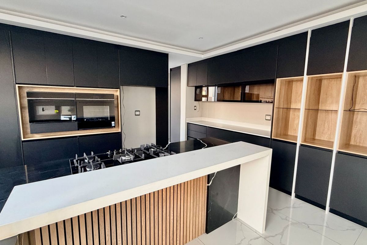 Modern kitchen featuring sleek matte black cabinetry, integrated oven, gas hob, stone countertops, and a stylish slatted wood island detail.