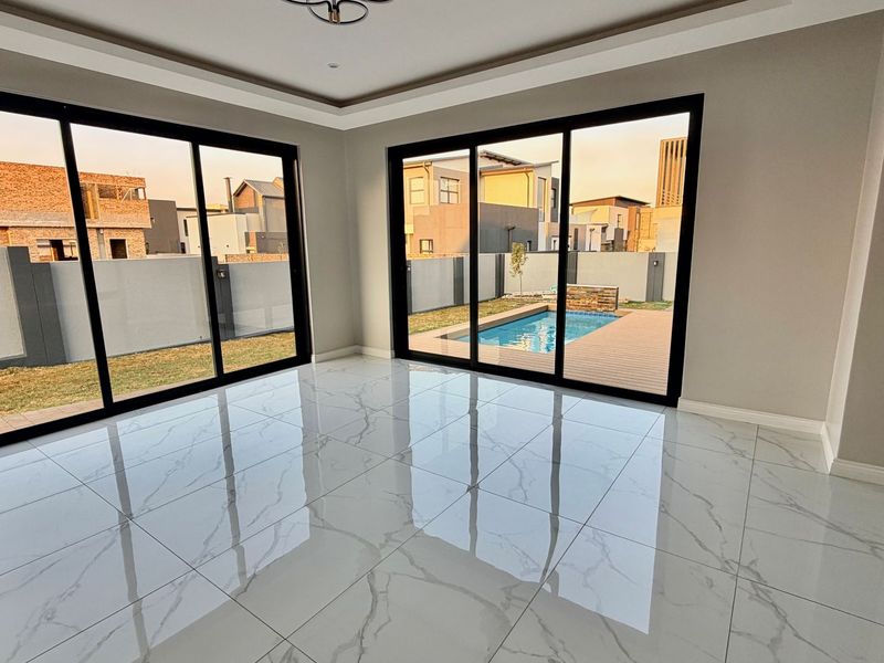 Spacious, modern living area featuring large format marble-look porcelain tiles, recessed ceiling details, and expansive sliding doors opening to a private pool and garden.