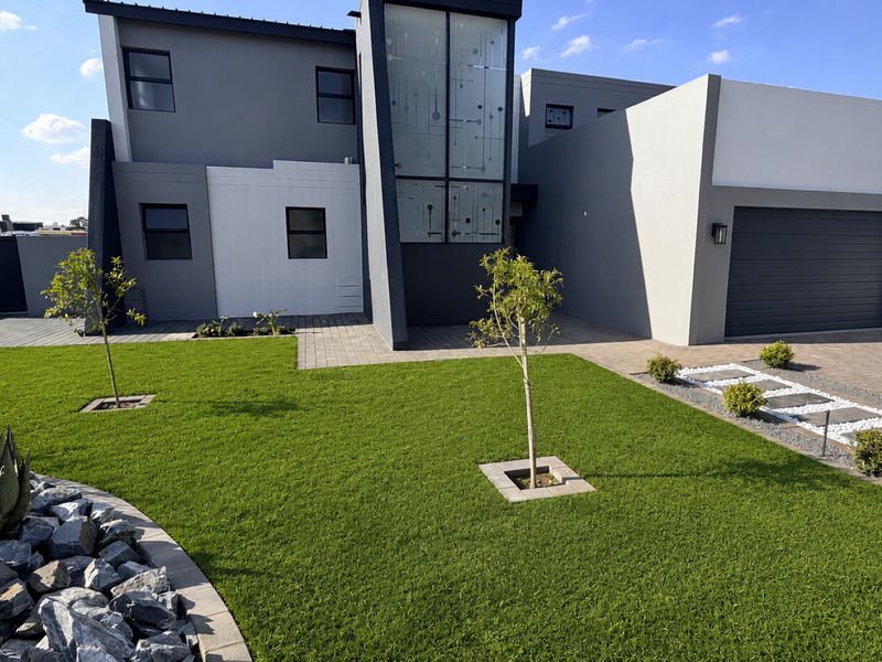 Modern double-story residential facade featuring a contemporary grey and white exterior, paved driveway, double garage, and well-maintained landscaped front garden.