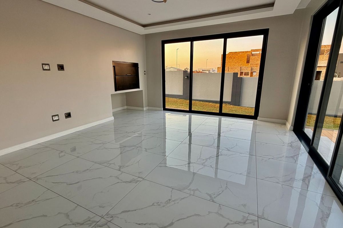 Modern, spacious living area featuring large format marble-look porcelain tiles, recessed ceiling detail, and sliding glass doors opening to the rear garden.