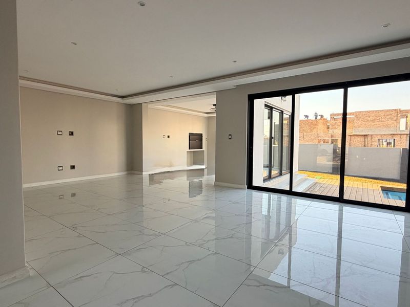 Spacious open-plan living area featuring large format marble-look porcelain tiles, recessed lighting, and expansive sliding glass doors leading to the outdoor patio.