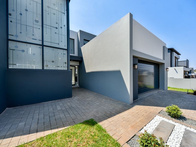 Modern front facade featuring a paved driveway, integrated garage, and striking decorative glass architectural detail.