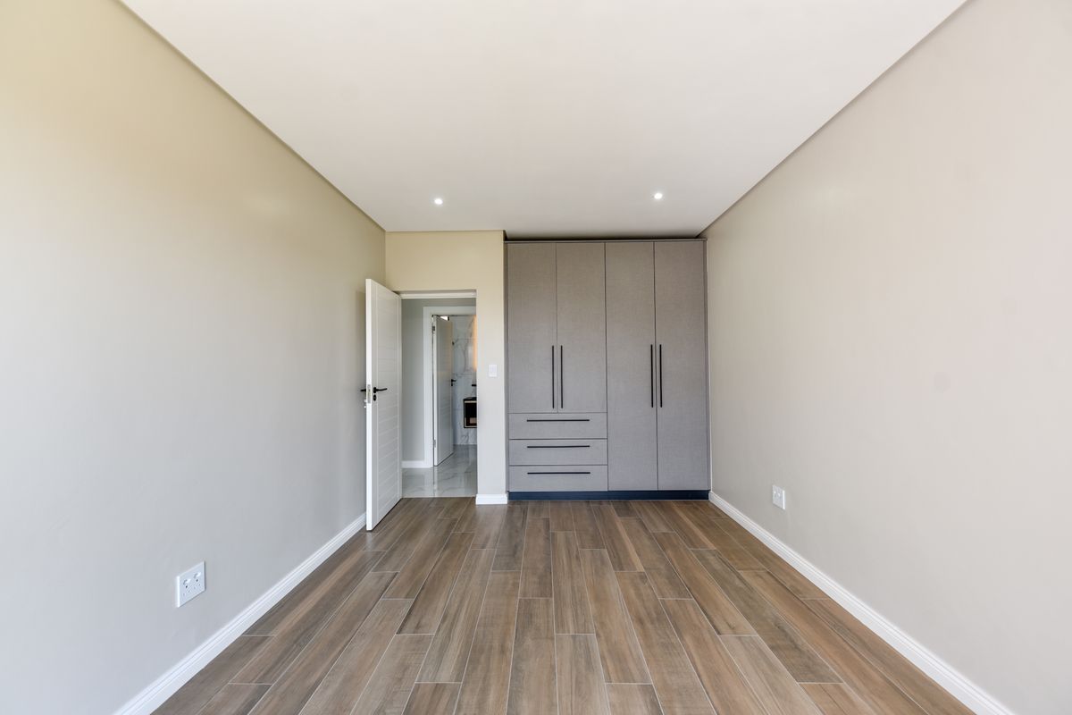 A bright, modern bedroom featuring wood-look tile flooring, neutral walls, and sleek built-in cupboards with contemporary hardware.