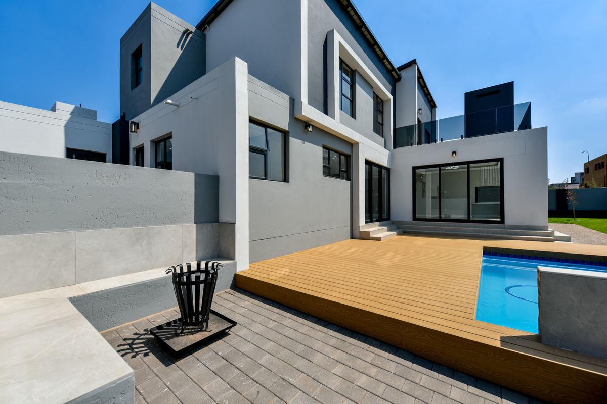 Modern rear exterior featuring a swimming pool, timber decking, paved patio area, and glass balustrade, seamlessly connected to the home via sliding doors.