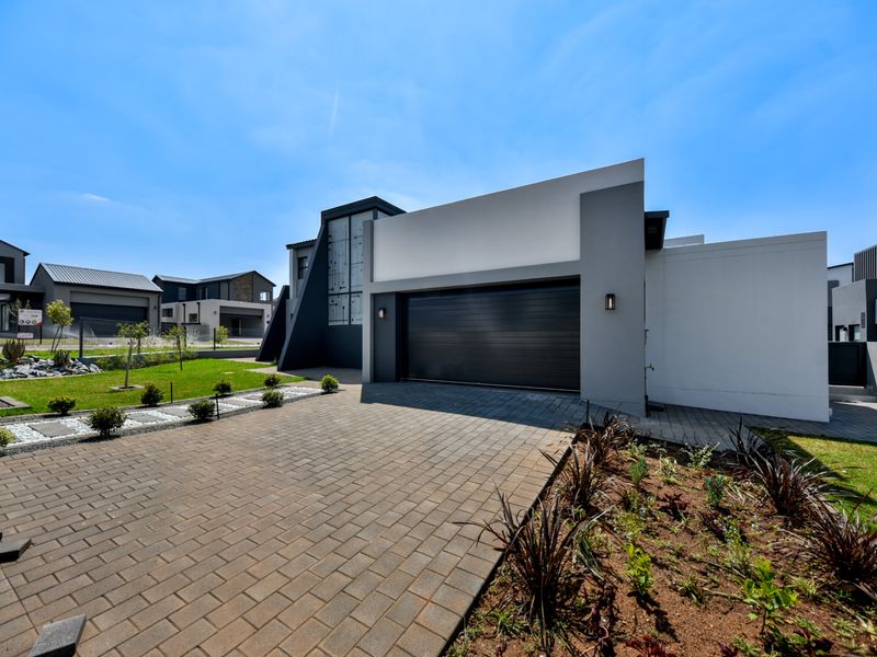Modern contemporary home exterior featuring a paved driveway, landscaped garden, and a sleek automated garage door.