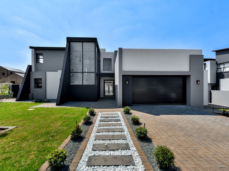 Modern double-story residence featuring a contemporary facade, paved driveway, integrated double garage, and a landscaped front garden with a stone walkway.