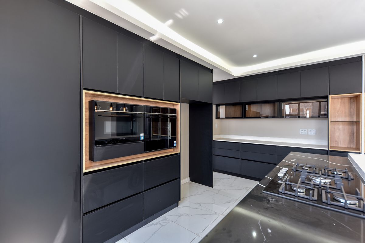 Modern kitchen featuring sleek matte black cabinetry, integrated appliances, stone countertops, a gas hob, and elegant marble-look flooring with recessed lighting.