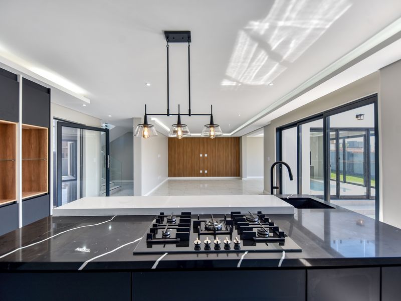 Modern open-plan kitchen and living area featuring a sleek island with gas hob, stone countertops, and elegant slatted wood wall accents.