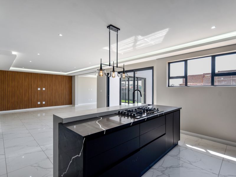 Modern open-plan living area featuring a sleek kitchen island with gas hob, stone countertops, and a stylish slatted wood feature wall.