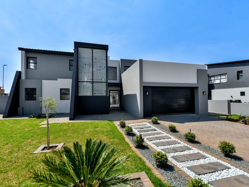 Modern double-story residential home featuring a contemporary facade, paved driveway, and a landscaped front garden with a stone-accented pathway.