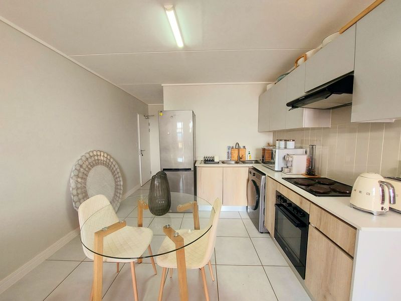 A modern open-plan kitchen featuring light wood-finish cabinetry, a built-in oven and hob, tiled flooring, and a functional layout.