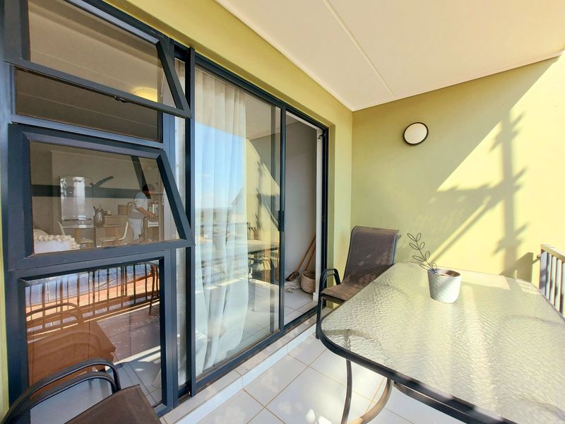 A covered balcony featuring tiled flooring, sliding glass doors providing access to the interior, and a wall-mounted light fixture.