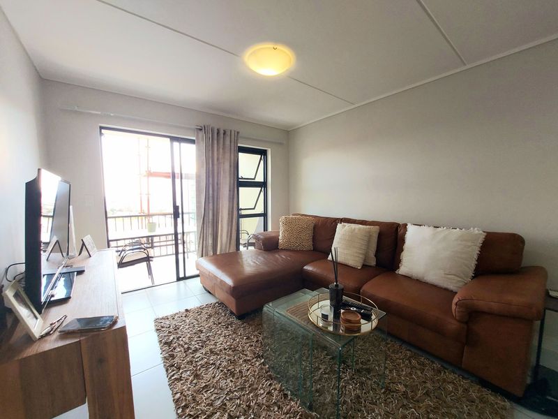 A bright living room featuring tiled flooring and a sliding glass door that provides access to an outdoor balcony area.