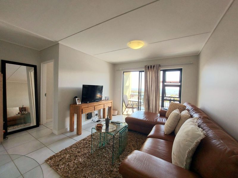 A bright living room featuring tiled flooring and a sliding glass door that provides access to an outdoor balcony area.
