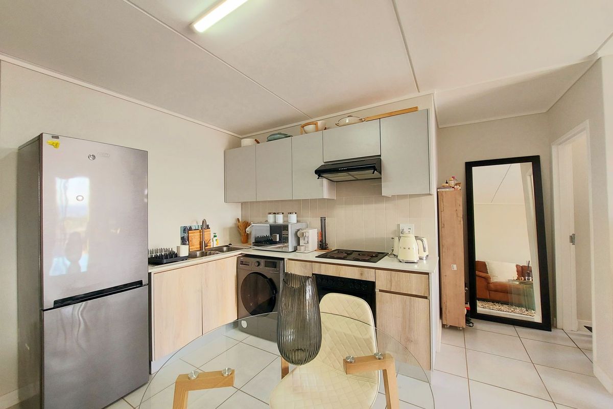 Compact kitchen featuring light wood-finish cabinetry, tiled backsplash, integrated electric hob, oven, and extractor fan, with tiled flooring throughout.