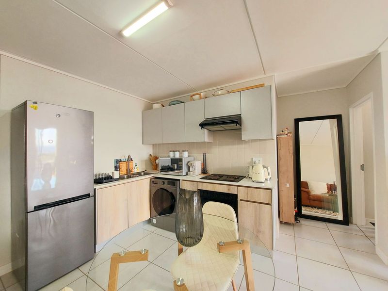 Compact kitchen featuring light wood-finish cabinetry, tiled backsplash, integrated electric hob, oven, and extractor fan, with tiled flooring throughout.