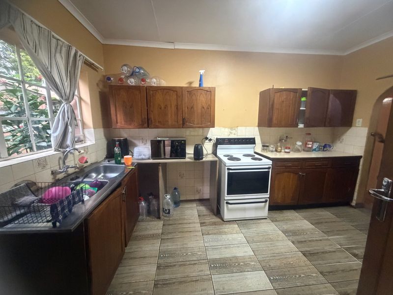 A functional kitchen featuring wooden cabinetry, a stainless steel double sink, and a freestanding electric stove with tiled flooring and backsplash.