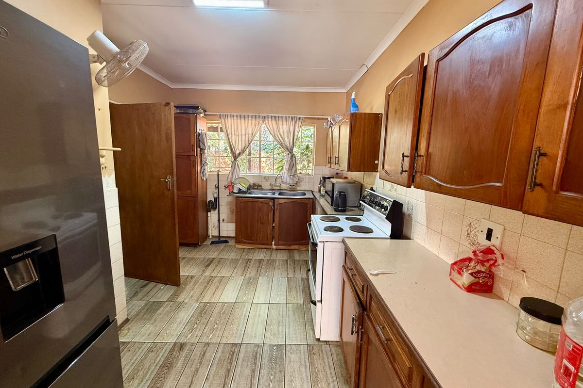 A functional kitchen featuring wooden cabinetry, tiled flooring, a double basin sink, and a freestanding stove with a tiled backsplash.