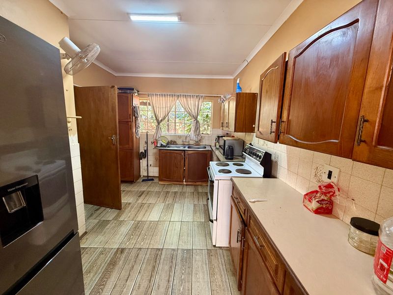 A functional kitchen featuring wooden cabinetry, tiled flooring, a double basin sink, and a freestanding stove with a tiled backsplash.