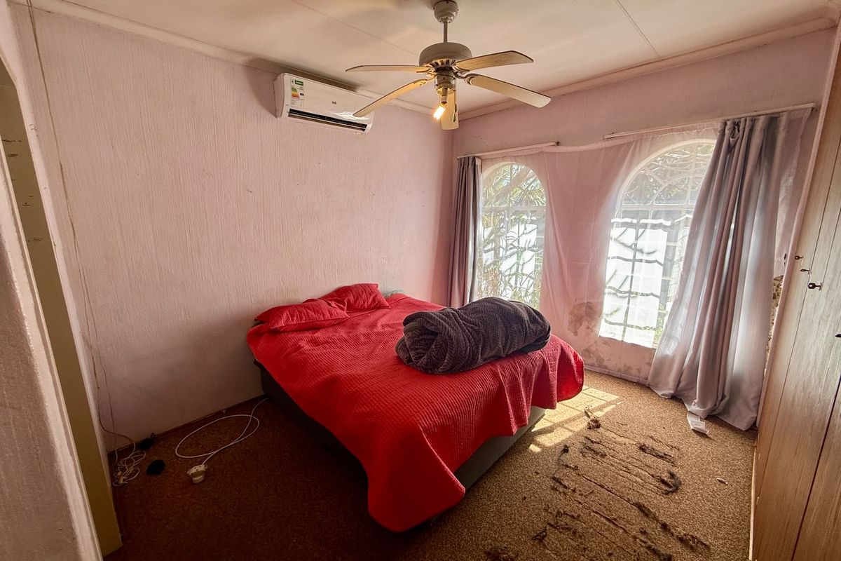 Bedroom featuring arched windows, a ceiling fan, and a wall-mounted air conditioning unit, requiring cosmetic updates and repairs to wall finishes and flooring.